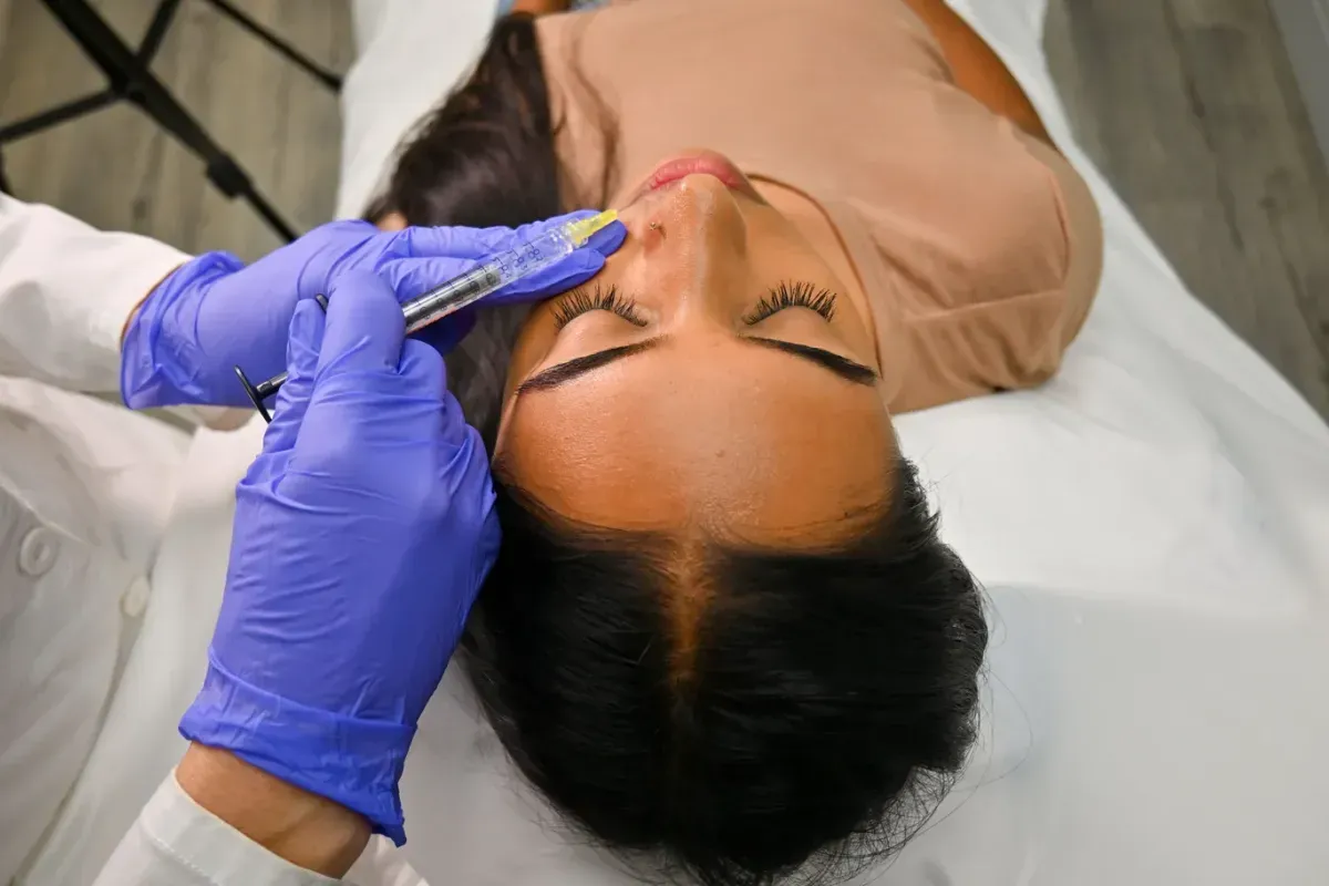 An injector treating a small spot beside a client’s nose, seen from above.
