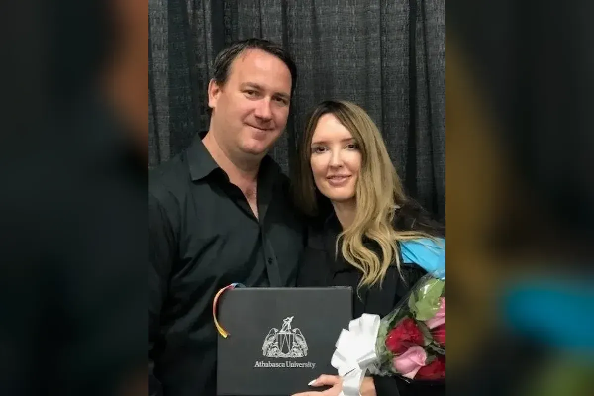 Michelle at her graduation, holding her Athabasca University diploma and a bouquet, with a guest beside her.