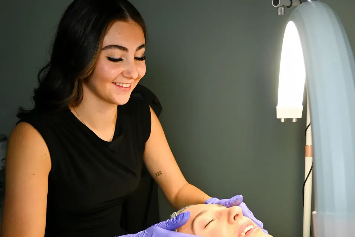 An aesthetician preparing a client’s skin under the treatment lamp.