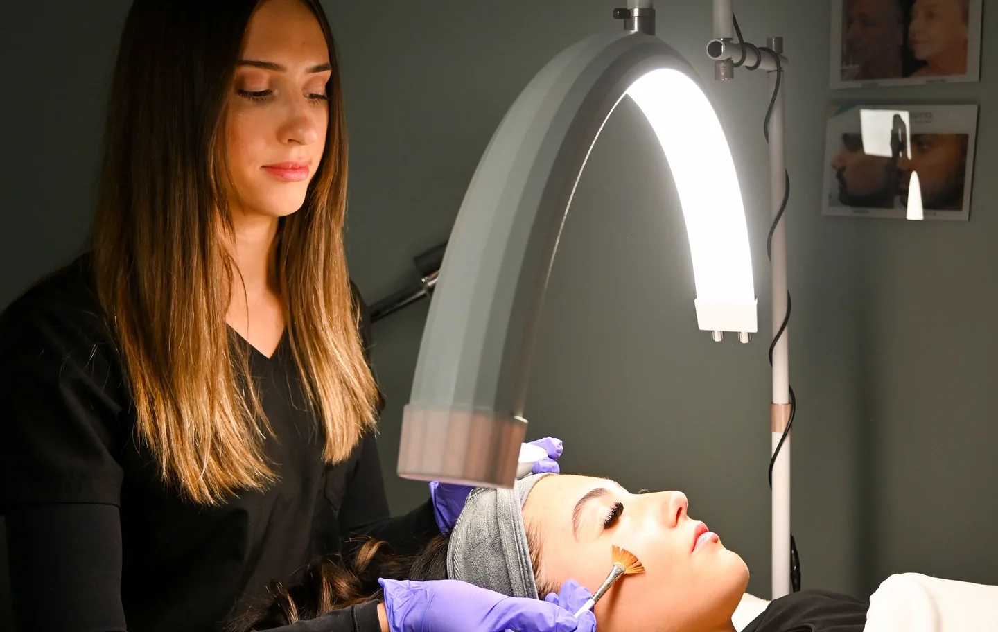 An aesthetician painting a peel onto a client’s cheek with a fan brush