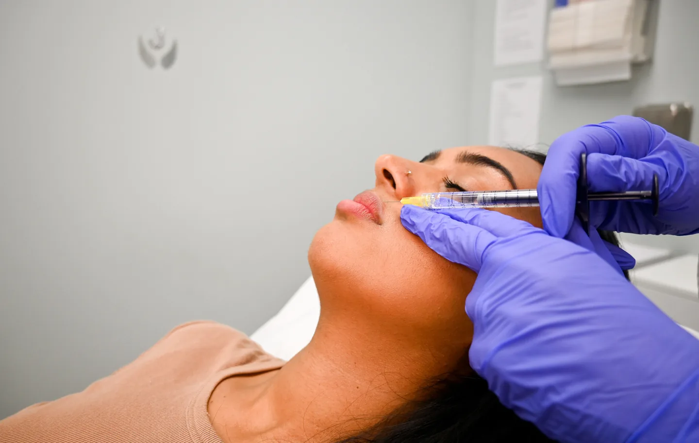 Gloved hands placing filler beside the nose and lip, side view