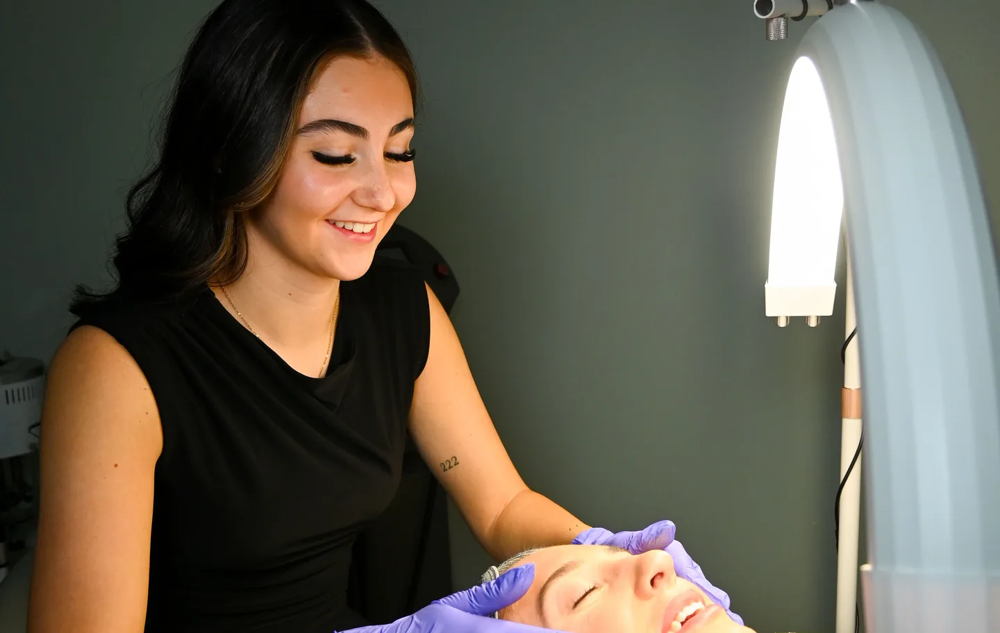 An aesthetician preparing a client’s skin under the treatment lamp