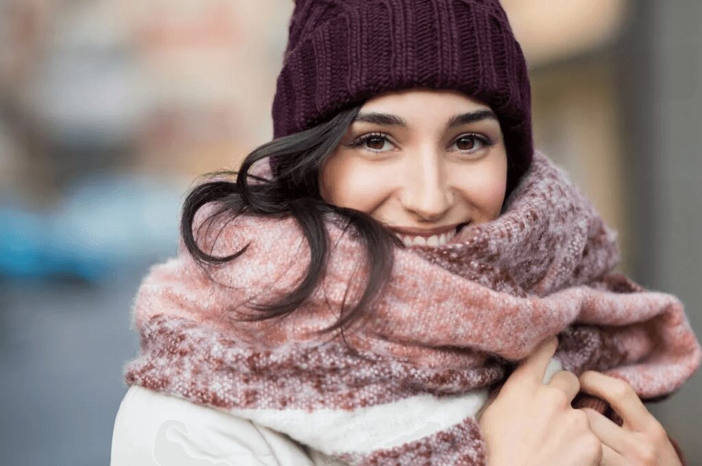 A woman wearing a scarf and beanie and smiling